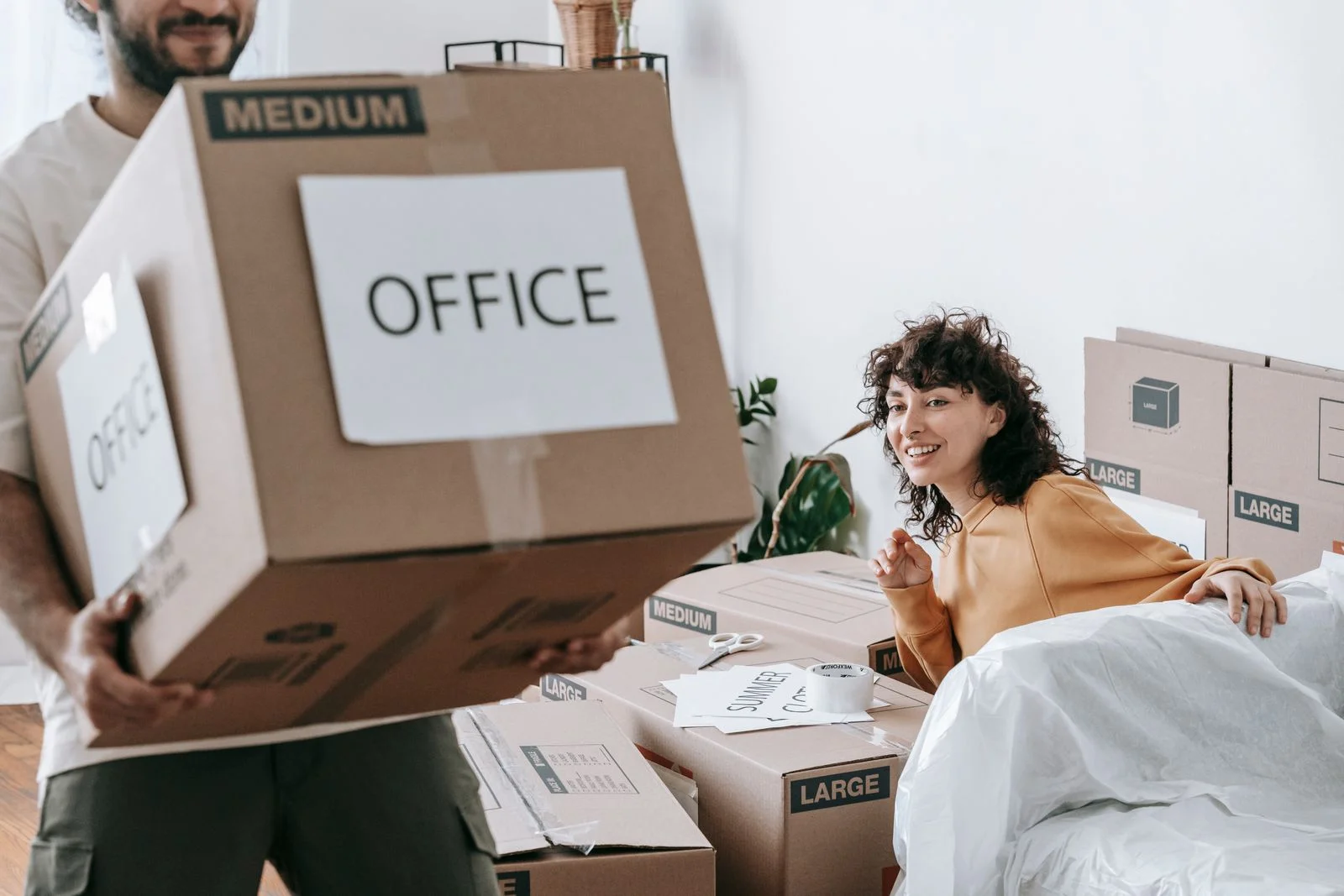 Ofis etiketi taşıyan karton kutuyla eşyalarını paketleyen iki kişi